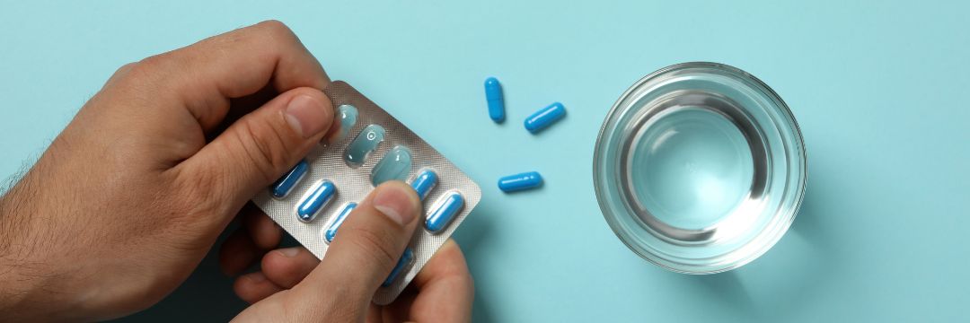 Man popping blue pills out of packaging next to glass of water