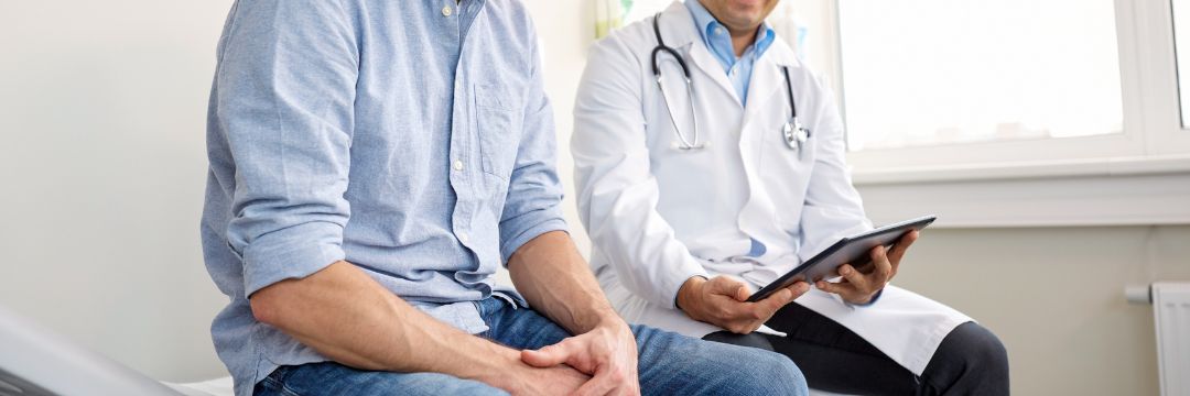 Man and doctor on doctors table in doctors office, doctor holding clipboard while male patients hands are in lap