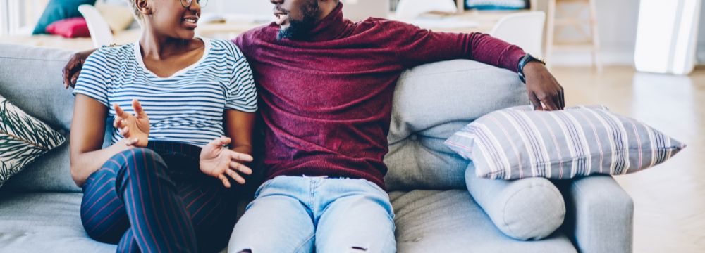 Couple having discussion on couch about penile implant options, man has arm around woman's shoulders