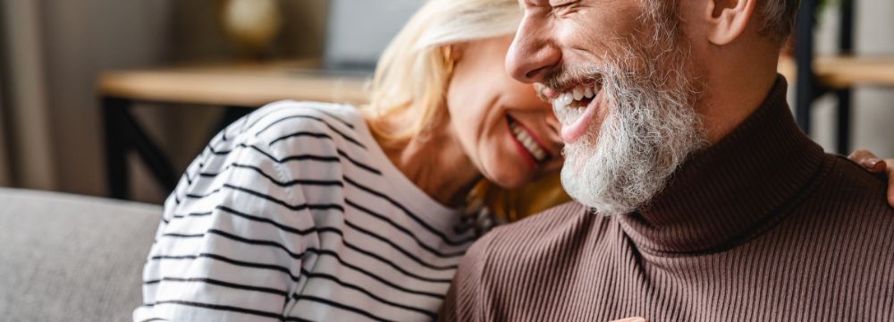 Older couple smiling and laughing, woman laughing into older man with beard shoulder